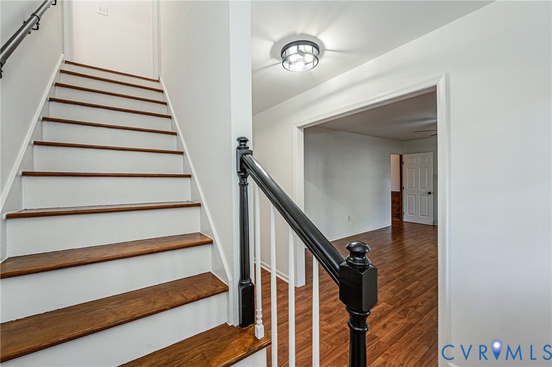 10100 Brittonwood Drive, Chesterfield, VA 23237 Staircase featuring wood-finish treads, white risers, and a black-finished handrail with white balusters, illuminated by a flush-mount circular ceiling fixture