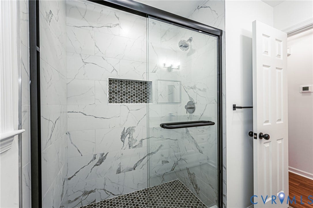 10100 Brittonwood Drive, Chesterfield, VA 23237 Walk-in shower featuring large-format white veined wall tile, a mosaic tile floor, an integrated wall niche, and a matte black frame glass enclosure