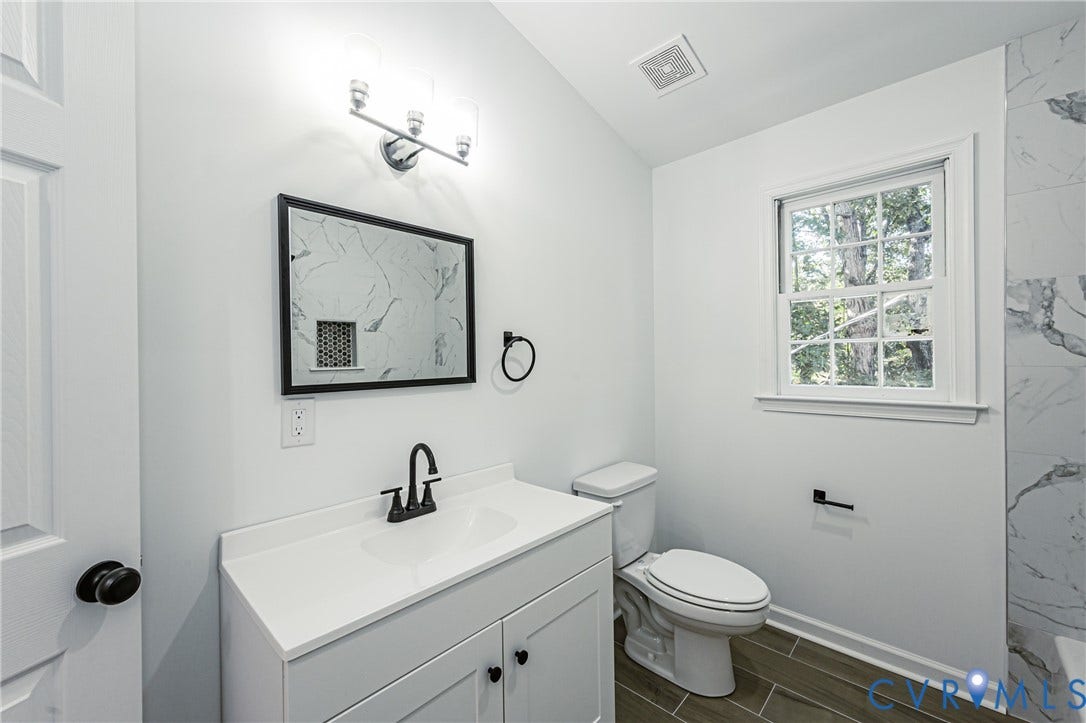 10100 Brittonwood Drive, Chesterfield, VA 23237 White vanity featuring a solid surface countertop, matte black faucet, framed mirror, and three-light vanity fixture, complemented by tile flooring and tiled wall accents