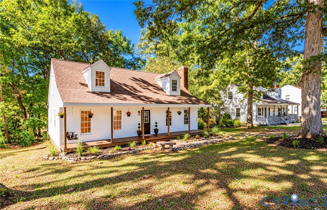 10100 Brittonwood Drive, Chesterfield, VA 23237 White-sided exterior featuring a covered front porch, dual dormer windows, a brick chimney, and rock-lined landscaping