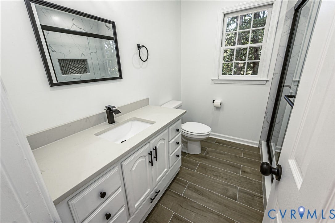 10100 Brittonwood Drive, Chesterfield, VA 23237 Bathroom featuring a white vanity with a composite countertop and integrated sink, matte black hardware, wood-finish tile flooring, a rectangular mirror with a black frame, and a shower with a glass enclosure