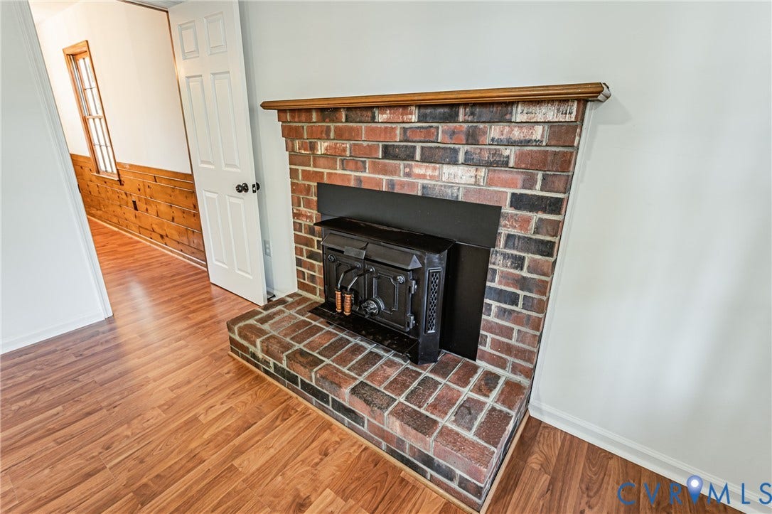 10100 Brittonwood Drive, Chesterfield, VA 23237 Multicolor brick fireplace featuring a wood-burning stove insert, raised brick hearth, and wood-finish mantle