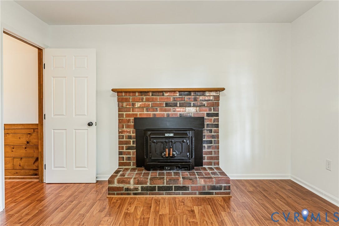 10100 Brittonwood Drive, Chesterfield, VA 23237 Multi-toned brick fireplace with a wood-finish mantel, integrated black metal stove insert, and wood-finish flooring