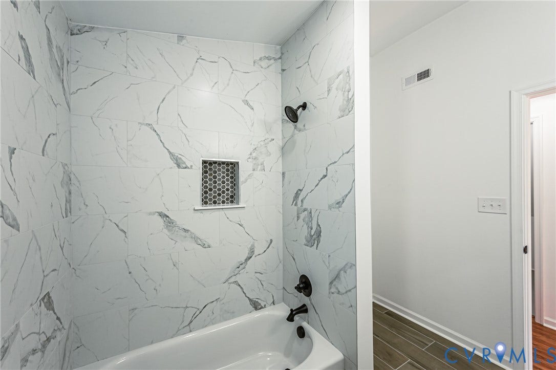 10100 Brittonwood Drive, Chesterfield, VA 23237 Bathtub with large-format stone-patterned wall tile, matte black hardware, and integrated hexagonal tile shower niche