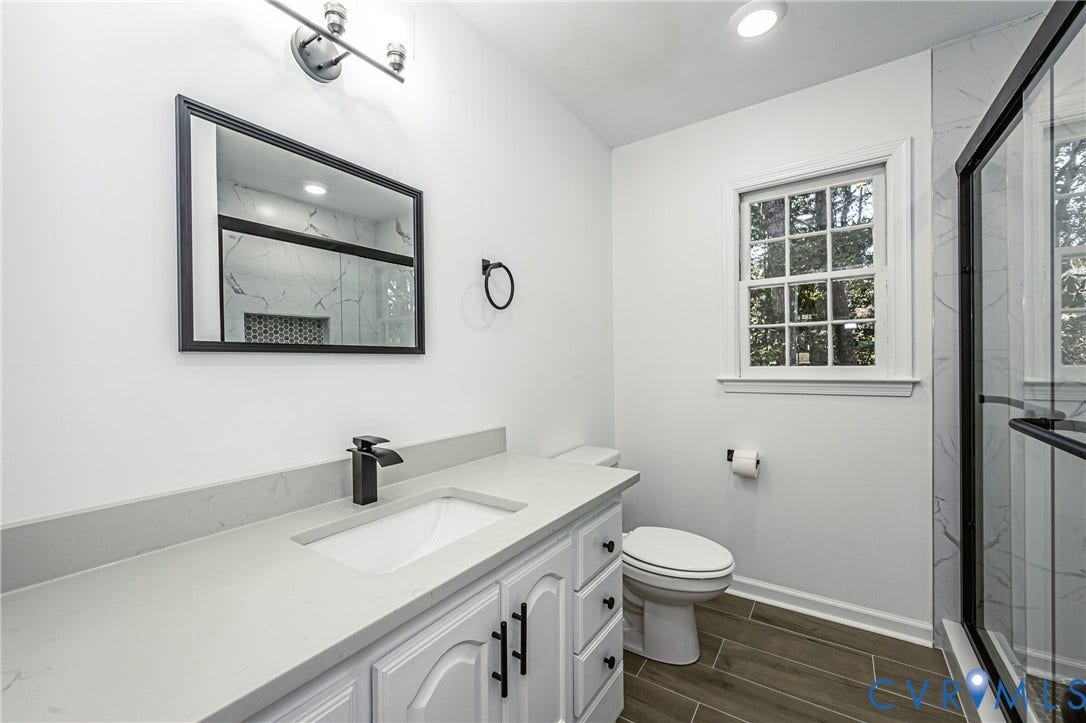10100 Brittonwood Drive, Chesterfield, VA 23237 Bathroom featuring a vanity with a light-toned solid surface countertop, rectangular undermount sink, matte black hardware, wood-finish flooring, and a walk-in shower with floor-to-ceiling tile surround
