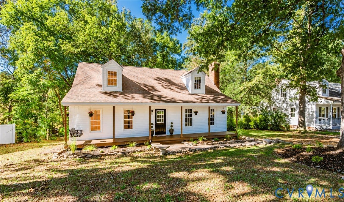 10100 Brittonwood Drive, Chesterfield, VA 23237 Cape Cod-style residence featuring white siding, a full-length covered front porch, dual dormer windows, a brick chimney, and a stone-lined landscaping bed