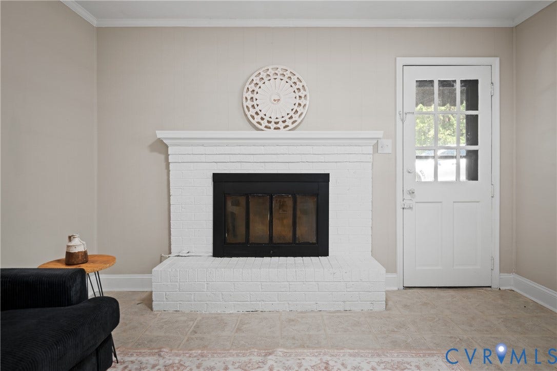 9010 Fawn Lane, Henrico, VA 23229 White brick fireplace featuring a black metal insert and a wide mantel, alongside a multi-pane glass entry door