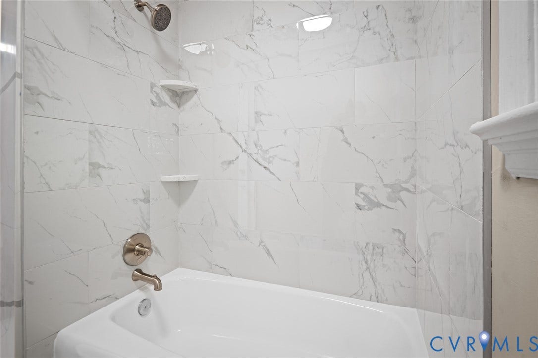 9010 Fawn Lane, Henrico, VA 23229 Full-height wall tiling with a veined pattern, integrated corner shelving, polished metal shower fixtures, and a porcelain soaking tub