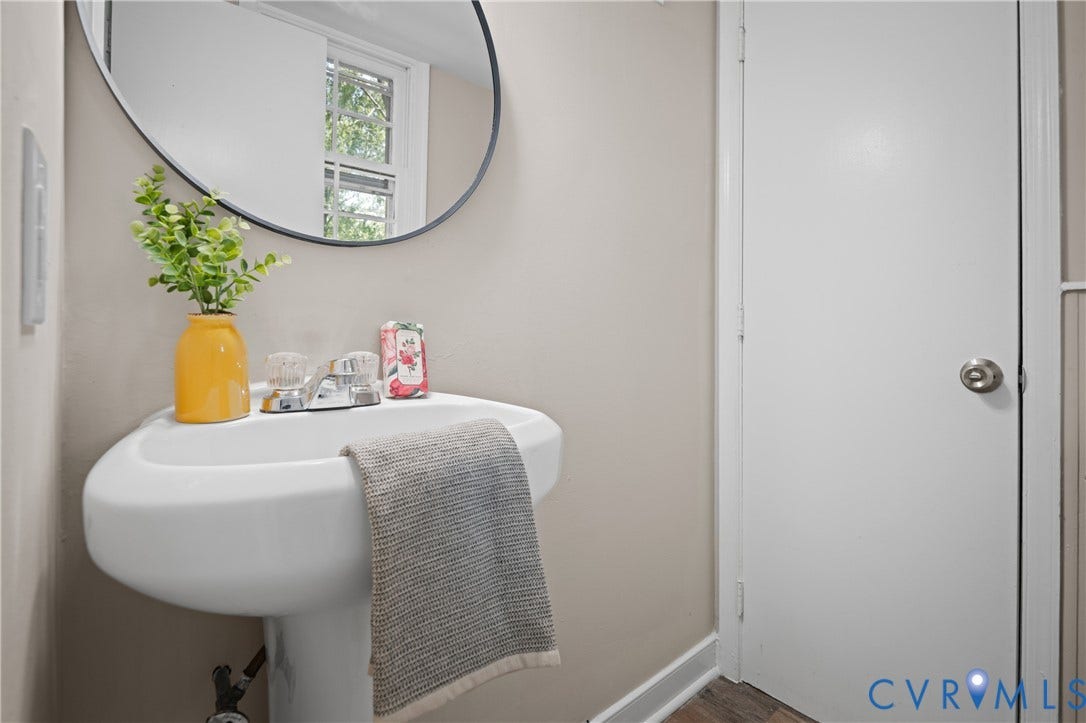 9010 Fawn Lane, Henrico, VA 23229 Corner-mounted pedestal sink featuring a chrome dual-handle faucet, oval wall-mounted mirror, and wood-finish flooring