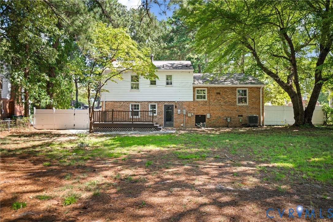 9010 Fawn Lane, Henrico, VA 23229 Rear exterior featuring a brick and white siding faade, elevated wood deck, and white privacy fencing on a wooded lot