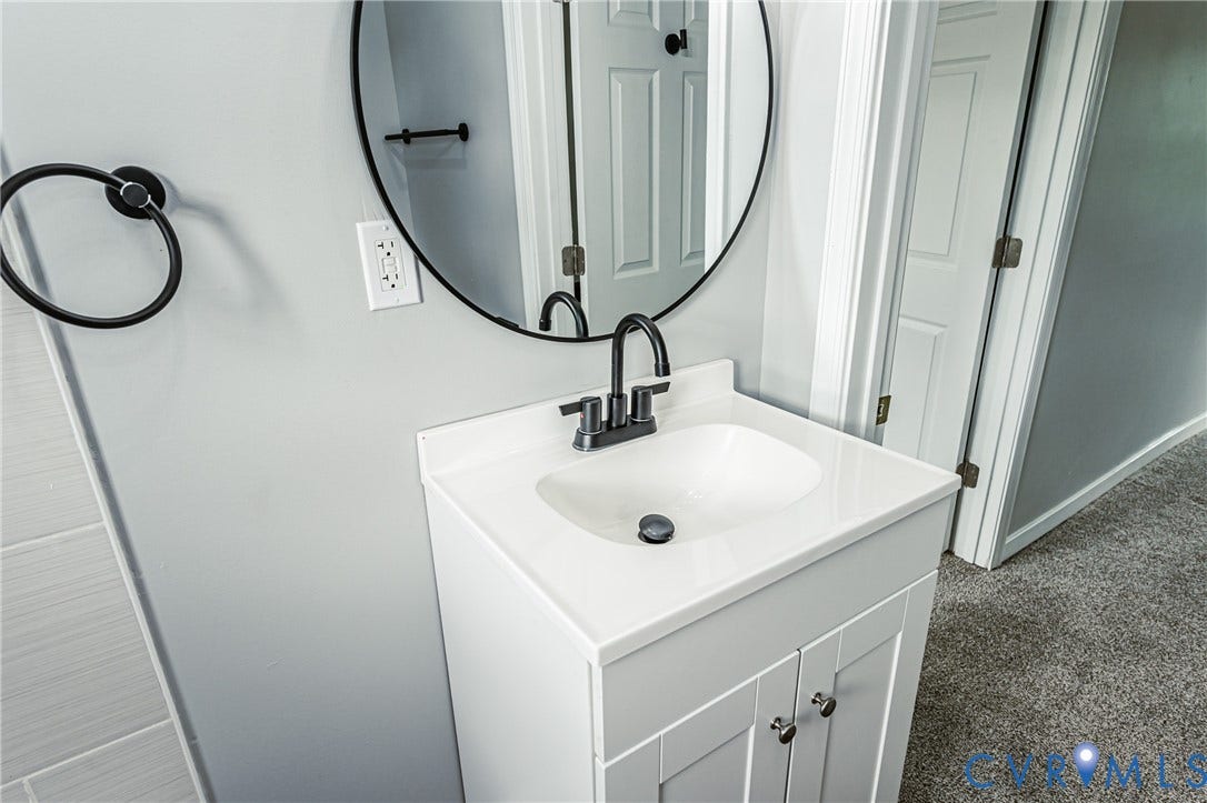 White vanity with a solid-surface countertop and integrated sink, matte black gooseneck faucet, circular mirror with a black frame, and coordinated matte black hardware