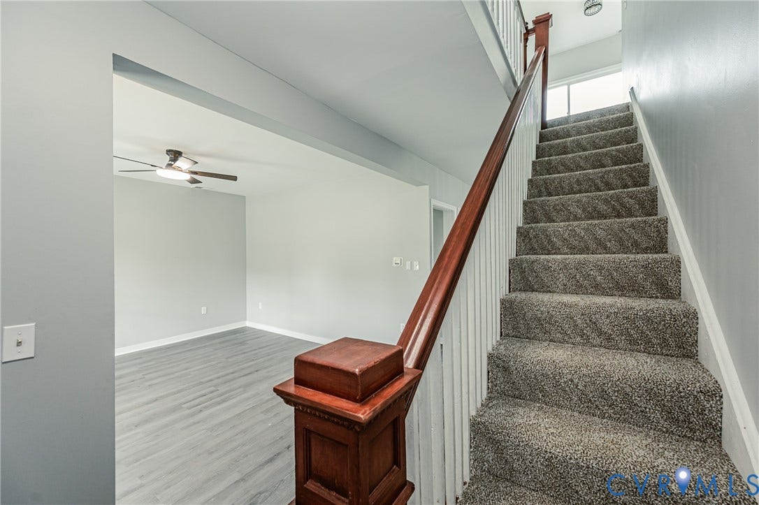 Staircase featuring wood-finish handrails, white balusters, and carpeted treads, complemented by wood-finish flooring and a ceiling fan