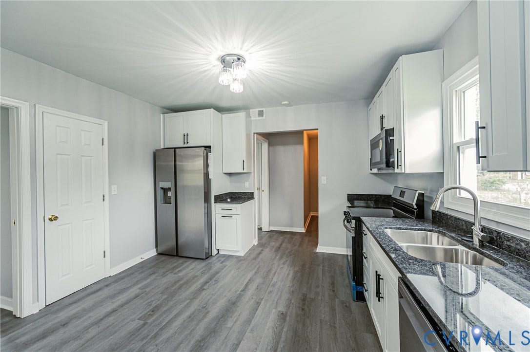 Kitchen featuring white shaker-style cabinetry, dark stone-finish countertops, stainless steel appliances, wood-finish flooring, and a dual-basin undermount sink with a high-arch faucet