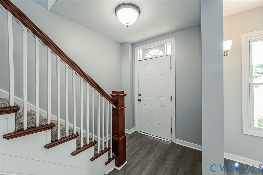 Entryway featuring wood-finish flooring, a staircase with a wooden handrail, white balusters, a paneled door with an arched transom window, and a flush-mount light fixture