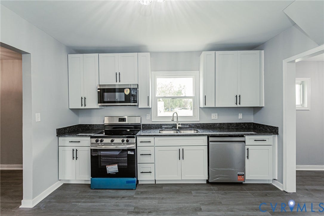 Kitchen featuring white cabinetry, dark stone-finish countertops, stainless steel appliances, and wood-finish flooring