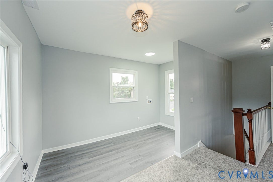 Neutral-toned interior featuring wood-finish flooring, recessed lighting, a decorative ceiling fixture, and a wooden staircase railing with white balusters