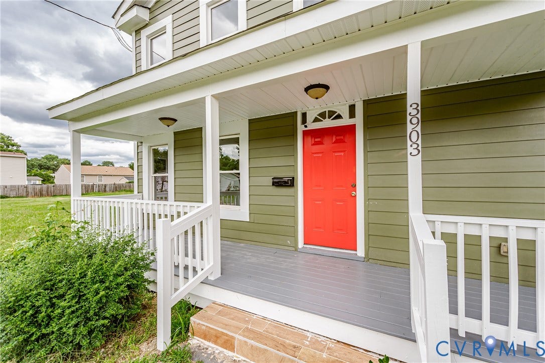Covered front porch featuring white railing, horizontal siding, tile-finished entry steps, and a red front door with a transom window