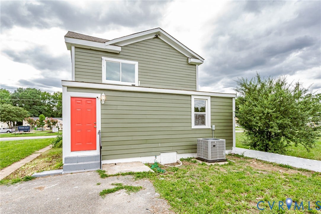 Two-story exterior featuring olive-toned horizontal siding, a red entry door, dual-pane windows, and an external HVAC unit