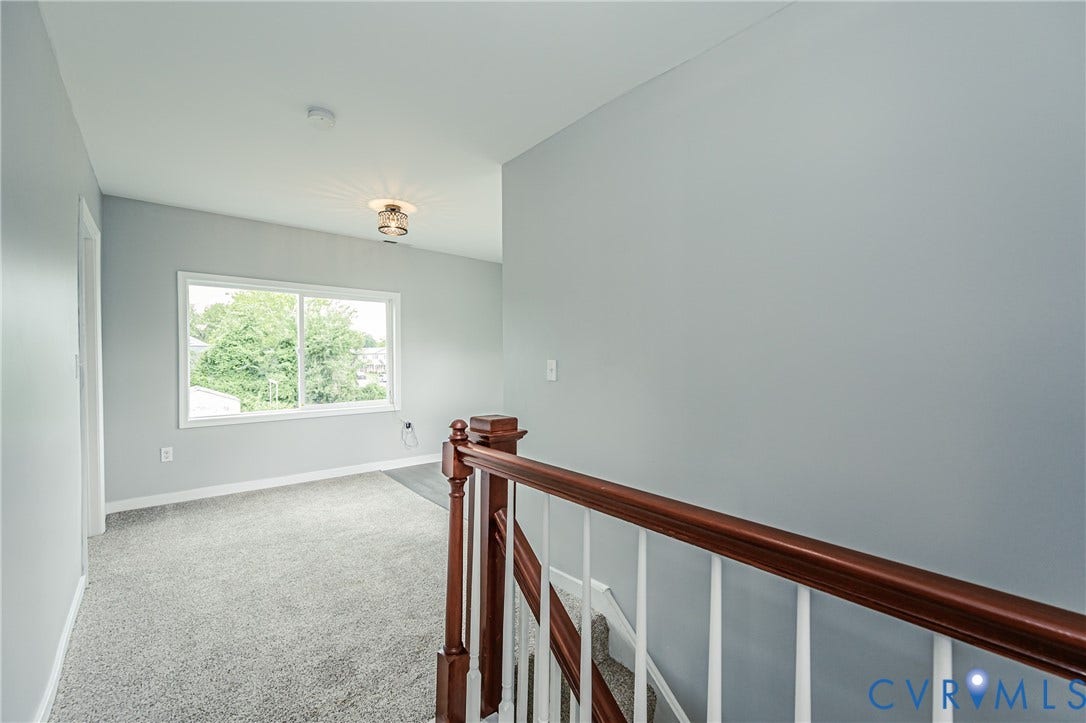 Staircase featuring a polished wood handrail with white balusters, neutral carpeting, and a flush-mount light fixture