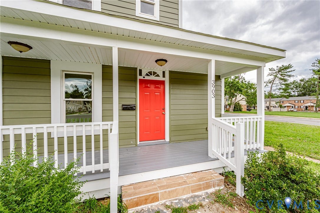 Covered front porch featuring horizontal lap siding, white wood railing, contrasting door, and tile steps