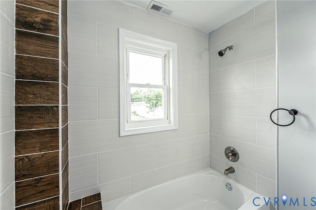 Full-height shower enclosure featuring light grey subway-style wall tiles, a wood-finish tile accent column, a built-in soaking tub, and brushed metal fixtures