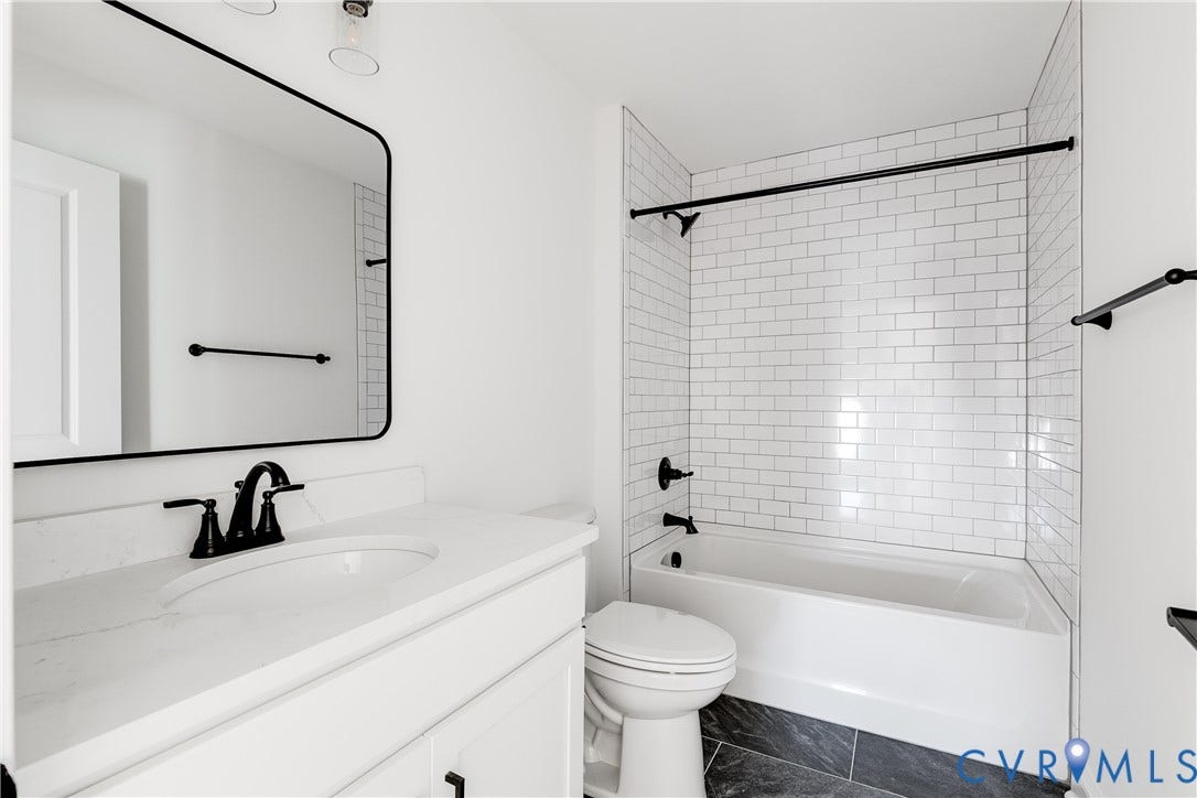 637 Ellens Haven Alley, Highland Grove, Richmond, VA 23222 Bathroom featuring a white vanity with a solid-surface countertop, rectangular mirror with a black frame, subway-tiled shower surround, matte black hardware, and dark stone-finish flooring