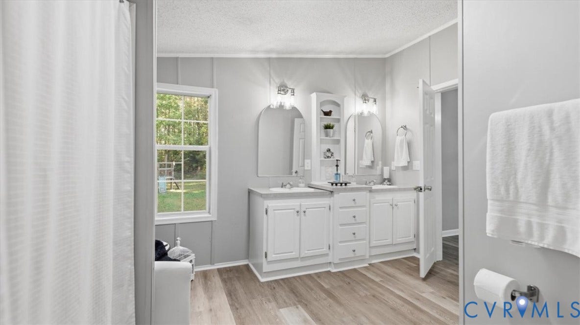 75 Claybank Road, Cumberland, VA 23040 Double vanity with white cabinetry, central tower shelving, two arched wall mirrors, and wood-finish flooring
