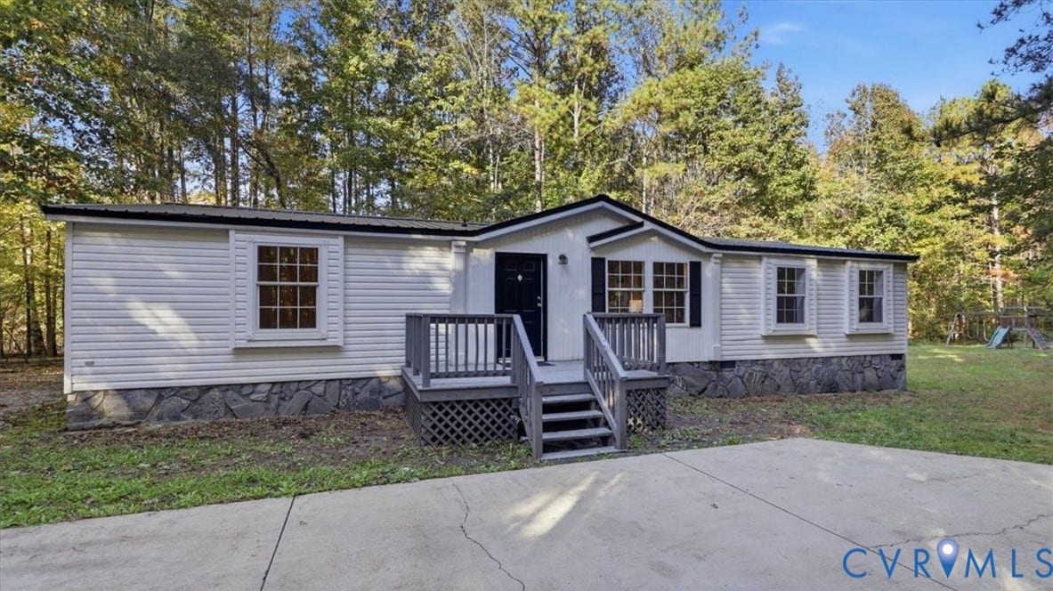 75 Claybank Road, Cumberland, VA 23040 Single-story exterior featuring white horizontal siding, stone-veneer skirting, a wooden deck with lattice foundation, and a concrete driveway