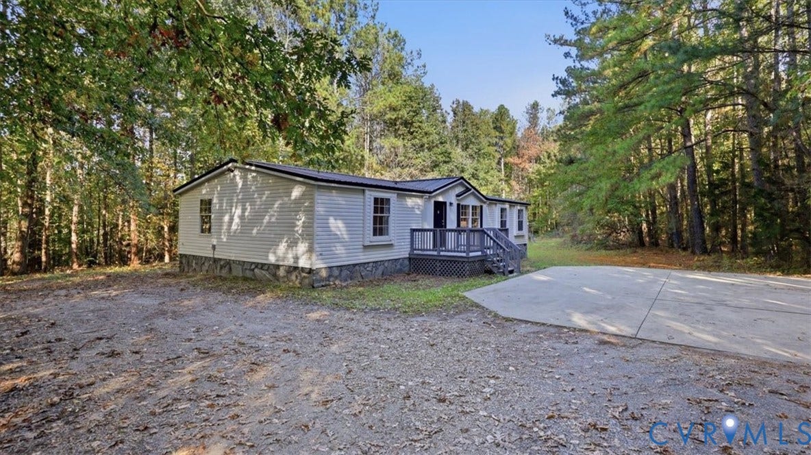 75 Claybank Road, Cumberland, VA 23040 Single-story residence featuring light-colored siding, stone-veneer skirting, a covered deck, and a paved concrete pad, situated on a wooded lot
