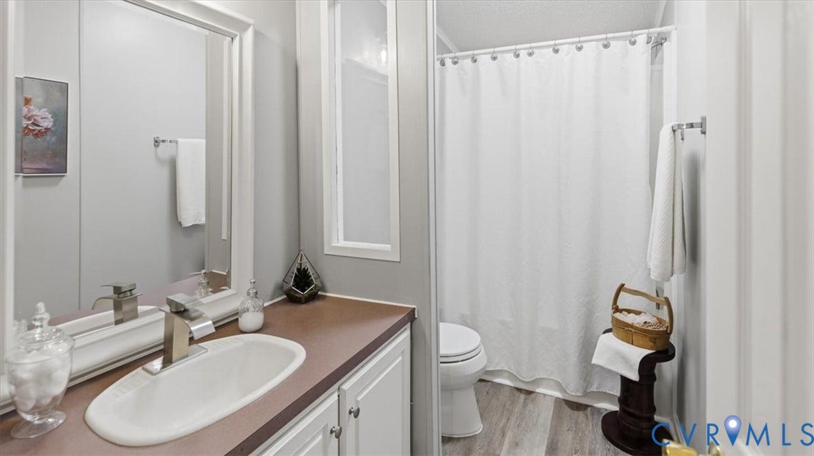 75 Claybank Road, Cumberland, VA 23040 Bathroom featuring a white vanity cabinet, rectangular under-mount sink with a chrome single-handle faucet, solid-surface countertop, and wood-finish flooring
