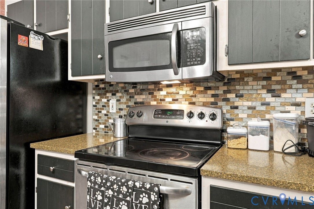 Kitchen featuring speckled stone countertops, mosaic tile backsplash, stainless steel microwave, and electric range with glass cooktop
