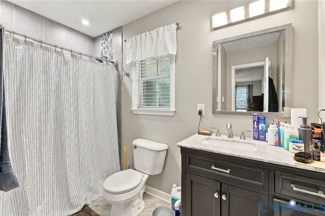 Dark-finished vanity cabinet with stone countertop, undermount sink, multi-light fixture, and tiled tub surround with mosaic accent detailing
