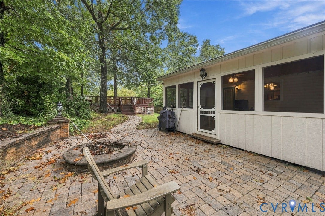 Paver patio featuring a built-in stone fire pit, retaining wall, screened-in porch, and elevated wood deck