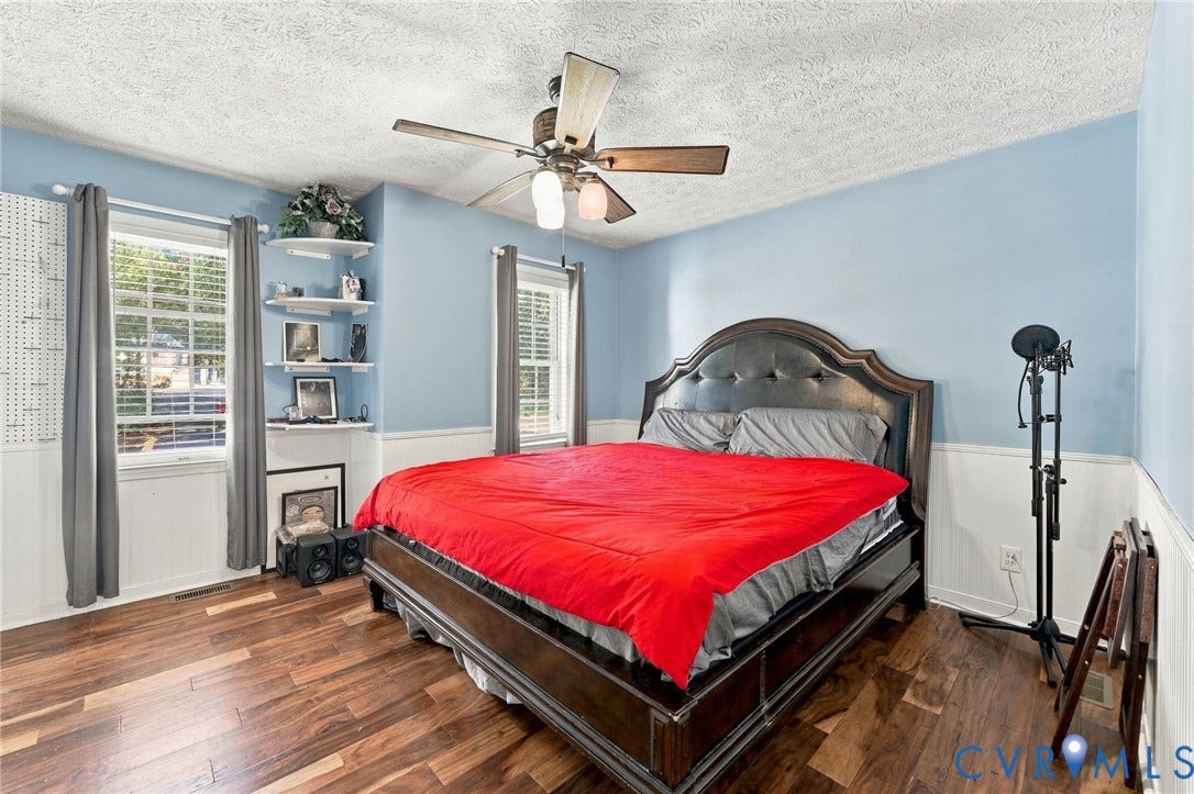 Room featuring wood-finish flooring, half-wall wainscoting, built-in corner shelving, multi-pane windows, and a ceiling fan with integrated lighting