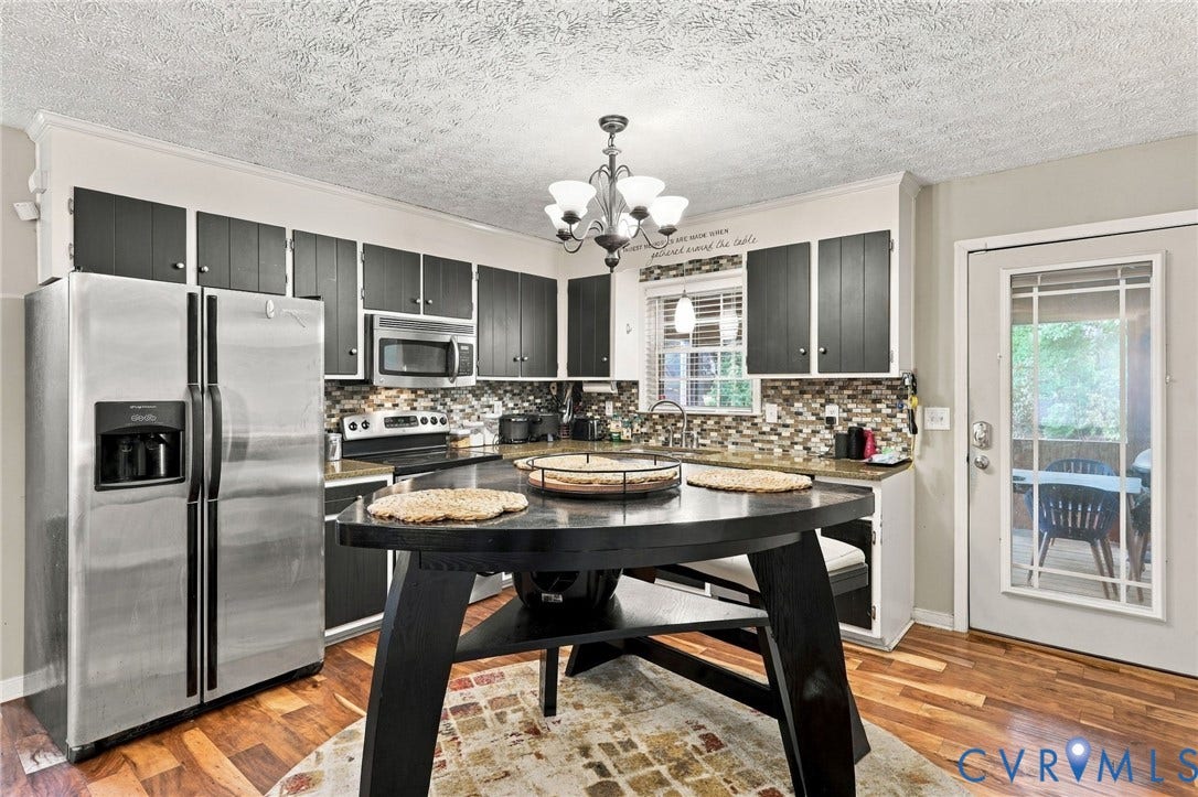 Kitchen featuring dark cabinetry, stainless steel side-by-side refrigerator, built-in microwave, stone tile backsplash, and wood-finish flooring