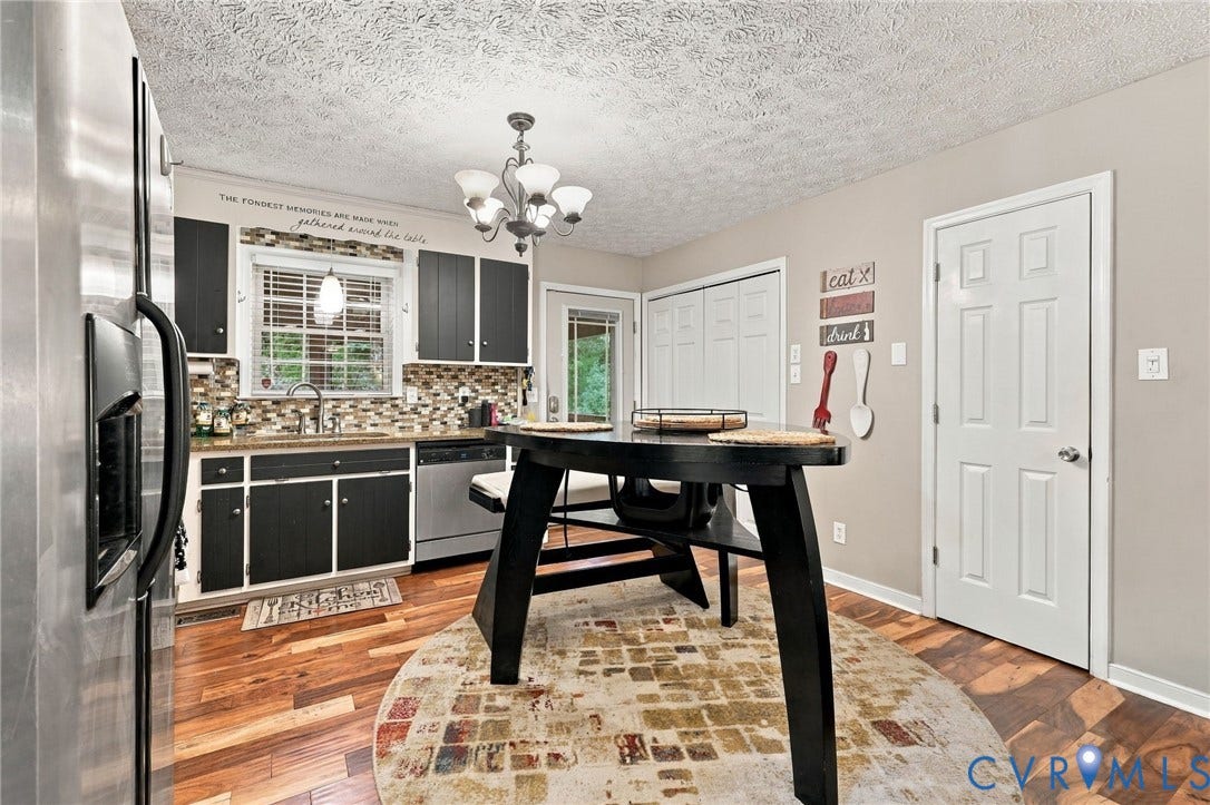 Kitchen featuring dark cabinetry, stone tile backsplash, wood-finish flooring, stainless steel dishwasher, and multi-light chandelier