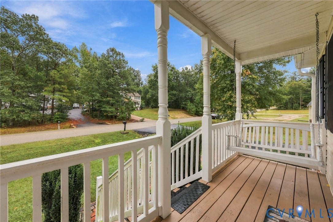 Covered front porch featuring wood-plank flooring, white railings, decorative support columns, and a suspended bench