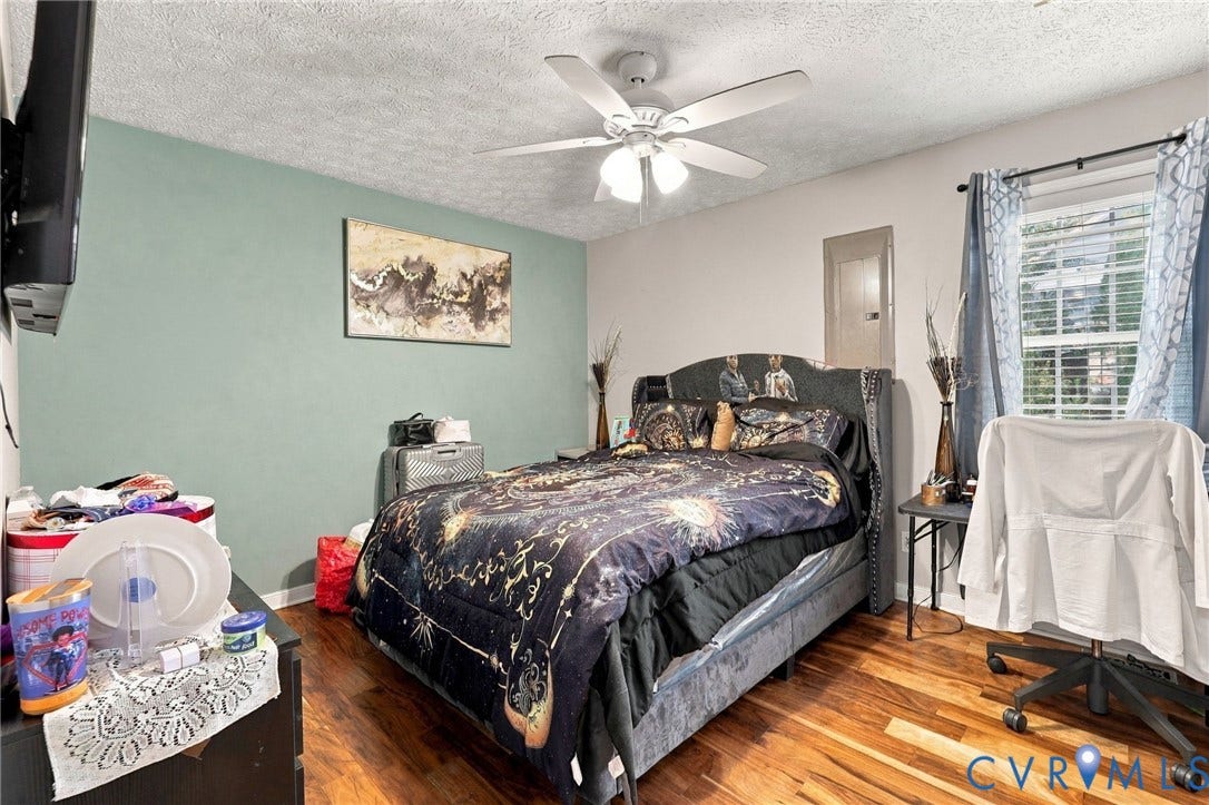 Room featuring wood-finish flooring, a sage green accent wall, and a multi-blade ceiling fan with an integrated three-light fixture
