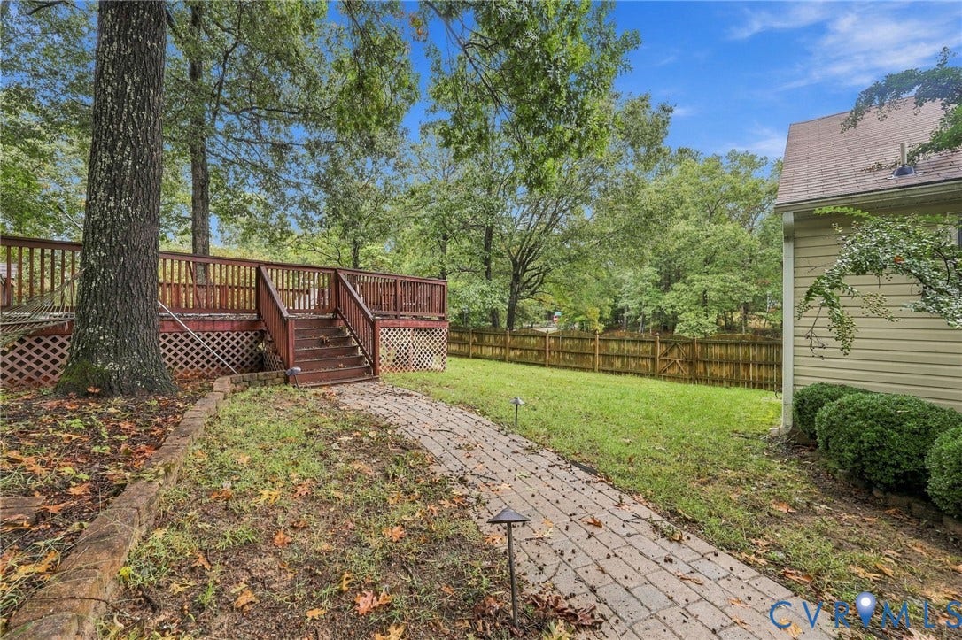 Rear yard featuring a raised wood deck with integrated stairs, a stone paver walkway, wood lattice skirting, and a perimeter wood privacy fence