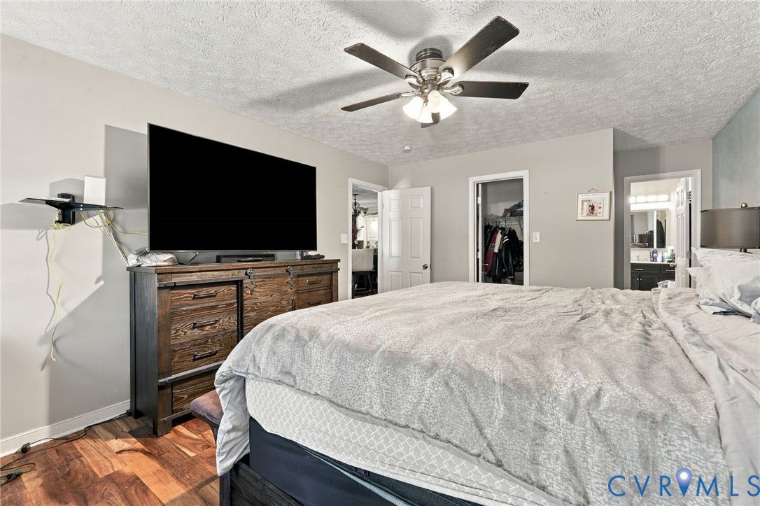 Neutral-toned interior featuring wood-finish flooring, a multi-blade ceiling fan with integrated lighting, and multiple interior doorways