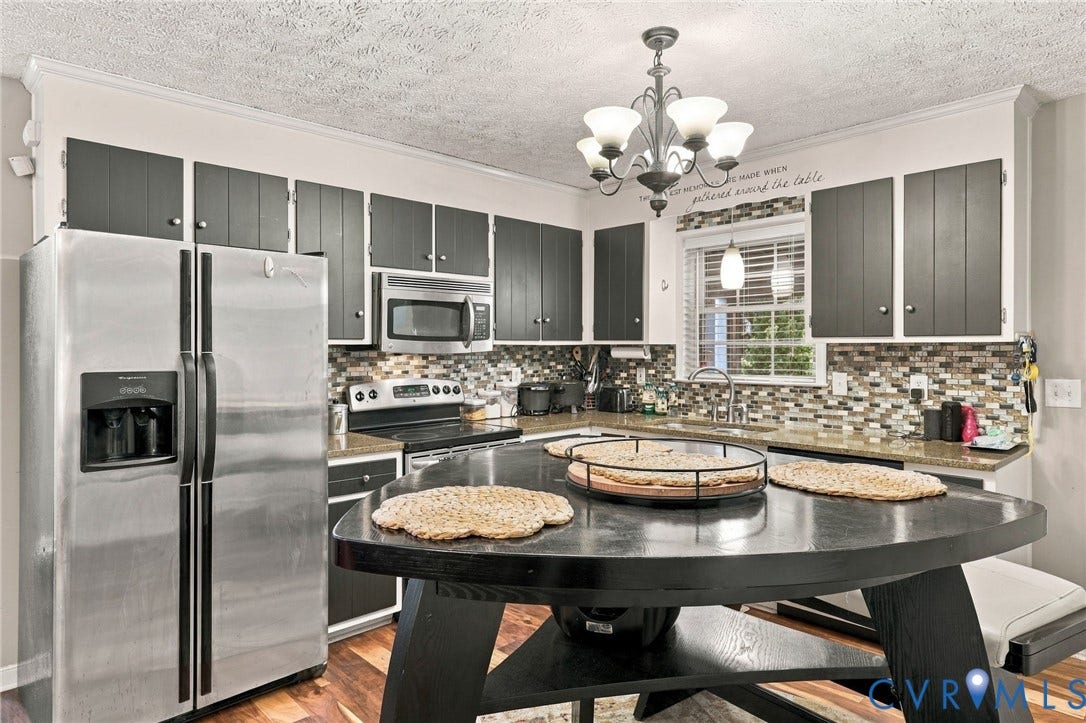 Kitchen featuring two-tone cabinetry, stainless steel appliances, multi-colored tile backsplash, stone-finish countertops, and an integrated multi-tiered island