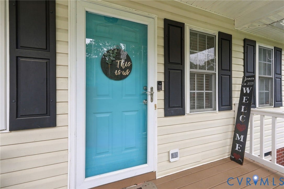 Exterior entryway featuring horizontal vinyl siding, black louvered shutters, a solid-paneled door, and a covered porch with a white railing