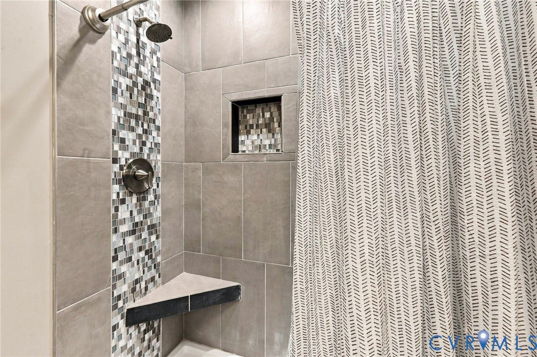 Shower featuring large-format ceramic tile, vertical decorative mosaic tile inlay, built-in corner bench, recessed niche, and polished chrome fixtures