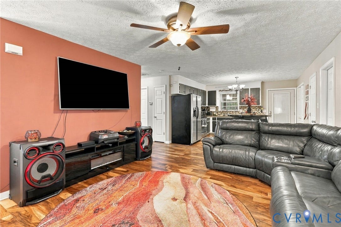 Open-concept space featuring wood-finish flooring, a ceiling fan with integrated lighting, and a prominent accent wall