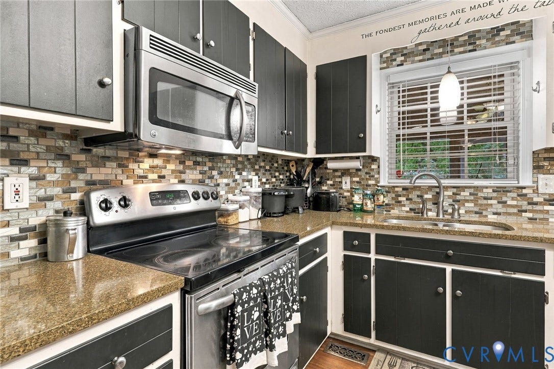 Kitchen featuring dark-finish cabinetry, stone-texture mosaic backsplash, stainless steel appliances, stone-composite countertops, and a single-basin undermount sink with a gooseneck faucet