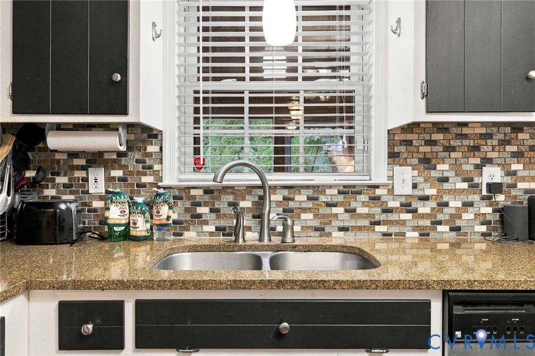 Dual-basin stainless steel sink with high-arc faucet, stone-composite countertop, multicolored mosaic tile backsplash, and two-tone shaker-style cabinetry