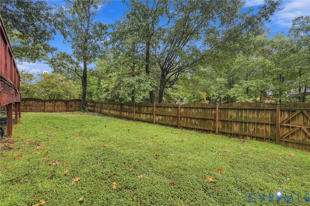 Backyard featuring a wood-finish fence, gated entry, grass lawn, and mature trees