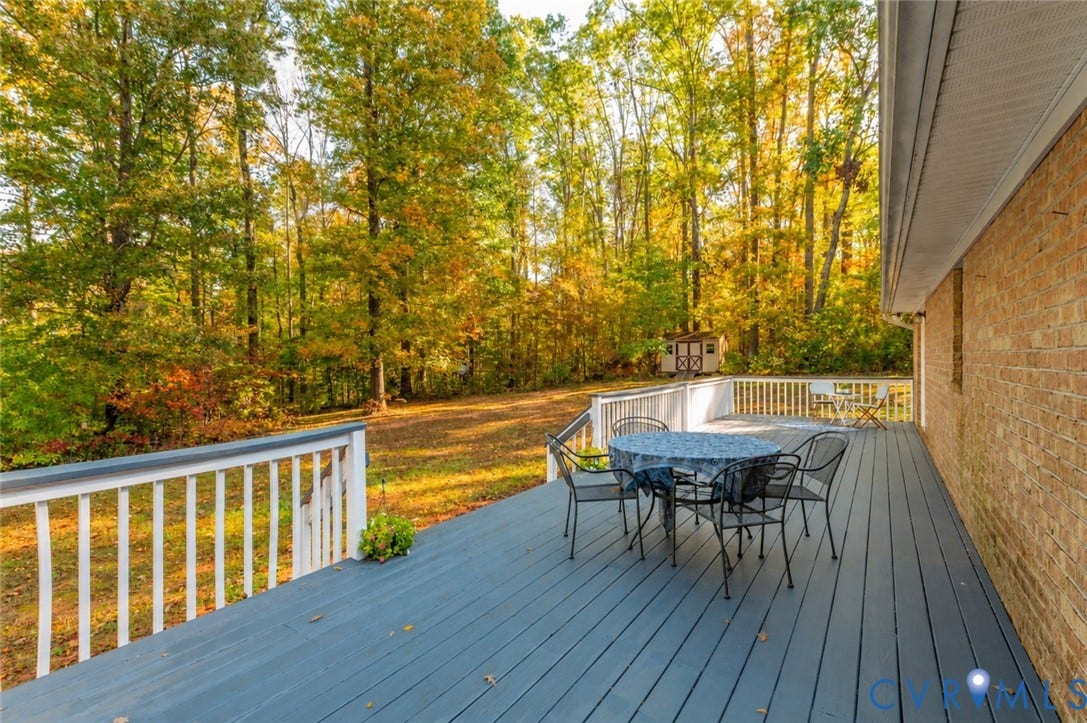3621 Jefferson Highway, Mineral, VA 23093 Expansive deck featuring painted wood-finish planks, white railings, and a brick exterior wall, set against a backdrop of mature trees