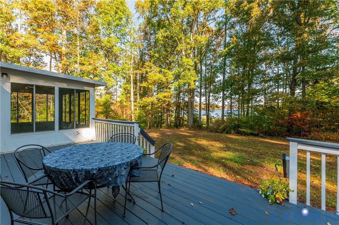3621 Jefferson Highway, Mineral, VA 23093 Painted wood deck featuring a white railing and an enclosed sunroom with large windows, overlooking a wooded yard and water