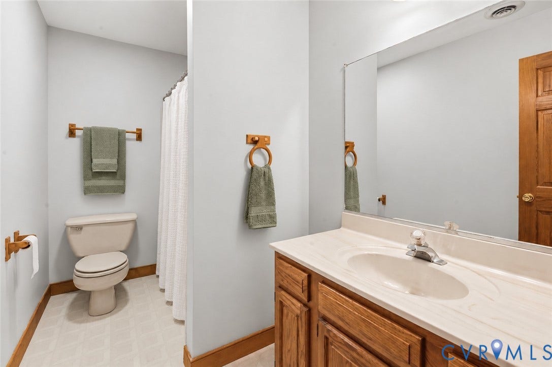 3621 Jefferson Highway, Mineral, VA 23093 Vanity featuring a wood-finish cabinet and integrated countertop with a molded sink, large wall-mounted mirror, and combination shower and tub enclosure